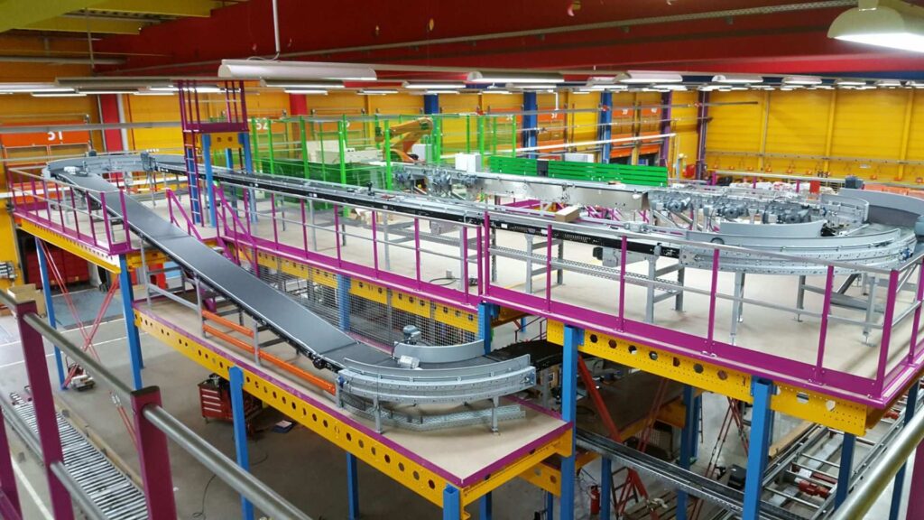 Overzicht van een modern magazijn met transportbanden en kleurrijke mezzanine-structuren.